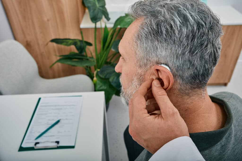 Audiologist fits a hearing aid on deafness mature man ear while visit a hearing clinic. Hearing solutions for older
